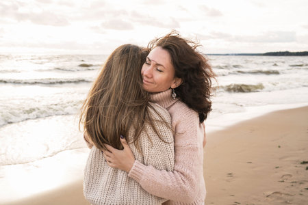 Cozy autumn walk of two girls on the shore of the windy sea. Adult sisters are trarking in blankets from the wind. A couple in love walks down the street and hugsの写真素材
