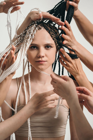 A beautiful girl with African pigtails looks into the frame. A lot of hands braided pigtails. A beautiful and strong girl is set up for good luck. A lot of hands near the girls faceの写真素材