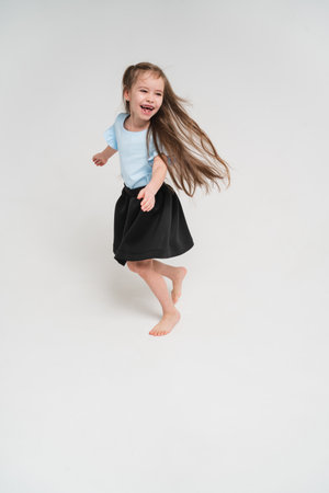 A little and sweet girl rejoices and dances. Baby in a blue T-shirt and black skirt. A child with very long hair. Happy child on a bright backgroundの写真素材