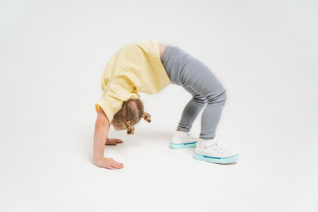 A girl in a yellow T-shirt and gray pants. A little girl is standing in a bridge. An athletic girl on a light background. Space for textの写真素材