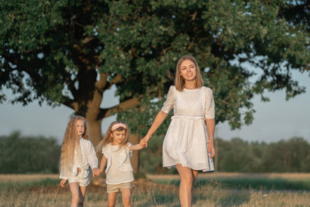 Harmonious relationship of mother with children. World Womens Day. Mom walks with the children in the village. Girls in a white dress with blonde hairの写真素材