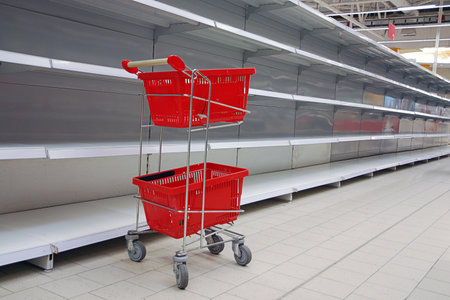 Shopping trolley with empty baskets by empty shelves in supermarketの写真素材