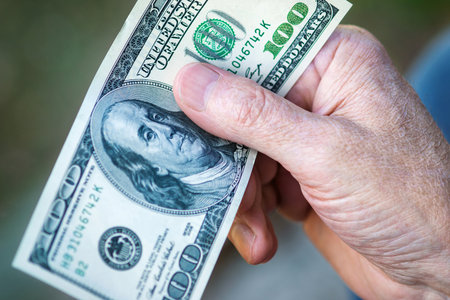 Hundred dollar bill in senior man's hand, close up