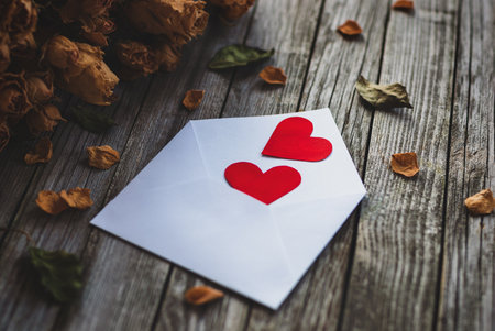 Two hearts in envelope, petals of dry roses on wooden tableの写真素材
