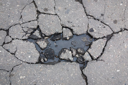 Large cracks on asphalt road filled with water, damage to the road surface in springの写真素材