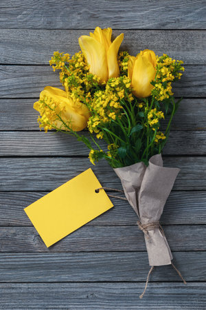 Bouquet of yellow flowers with blank paper card as a tag for name or greetings on wooden backgroundの写真素材