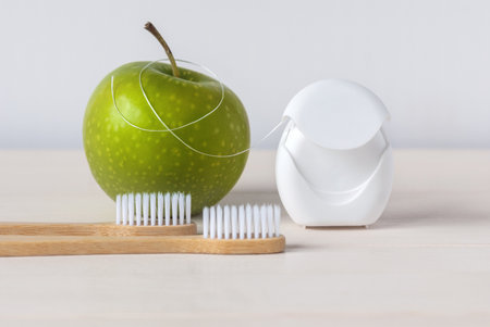 Bamboo toothbrushes, green apple and dental floss on white background - dental care routine to keep healthy teethの写真素材