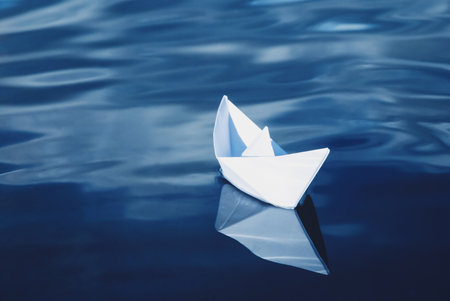 white paper boat floating in blue seaの写真素材