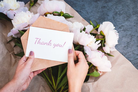 Thank you card in hands, message, envelope, pink peony flowers bouquetの写真素材