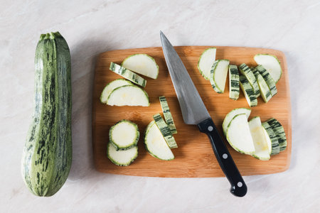 Cutting zucchini on wooden board, whole squash, knife and slices, overhead viewの写真素材