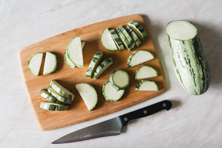 Zucchini cut into slices on cutting board, half squash, knife on white table, overhead viewの写真素材