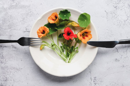Nasturtium plants, Indian cress flowers and leaves in plate on kitchen table, top viewの写真素材