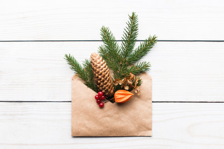 Christmas tree branch cone flowers decoration in paper envelope on white wooden background