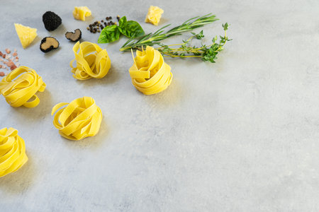 Raw italian fettuccine pasta with black truffles, herbs (basil, rosemary, thyme), slices of parmesan cheese and black pepper lies on a gray concrete background. Close-upの写真素材
