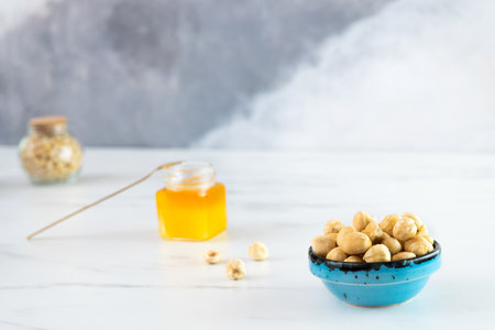 Peeled roasted hazelnuts in a blue bowl stands on a white plate. Nearby there is a small glass jar...