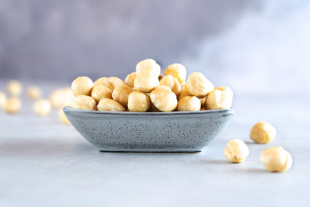 A full gray rectangular bowl of peeled hazelnuts stands against a light gray concrete background. There are several nuts nearby. Healthy food high in protein, omega-3s, antioxidants and vitamins. Close-upの写真素材