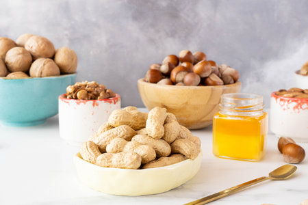 Different nuts in beautiful wooden and ceramic bowls (cashews, hazelnuts, walnuts) stand on a white...
