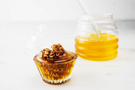 Walnuts with honey in a beautiful glass form stand on a white background. In the background is a transparent jar of honey. Close-up, selective focusの写真素材