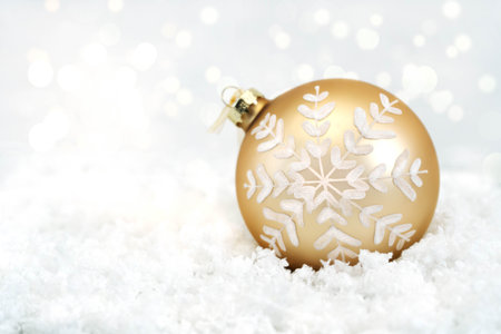 Christmas gold glass ball with a white pattern lies on white snow. Decoration for a Christmas tree on a white background. Bokeh in the background. Close-upの写真素材