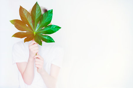 a teenage boy holds a large leaf from a tree in front of him on a light background