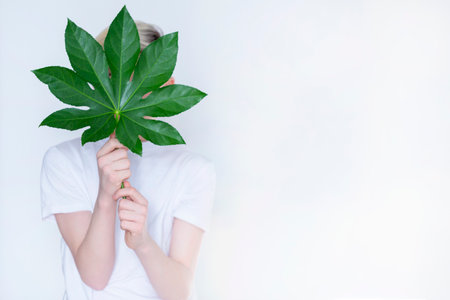a teenage boy holds a large leaf from a tree in front of him on a light background