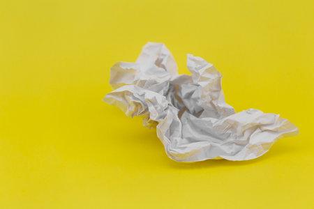 crumpled sheet of white paper on yellow background close-upの写真素材