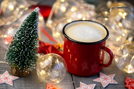 red coffee Cup illuminated with Christmas garland with Christmas decor close up