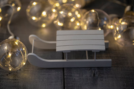 decorative white sledge, illuminated by a garland on a wooden surface close-upの写真素材