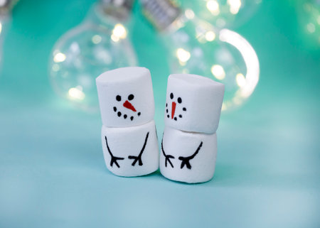 marshmallow snowman on mint turquoise background with garland lighting close up