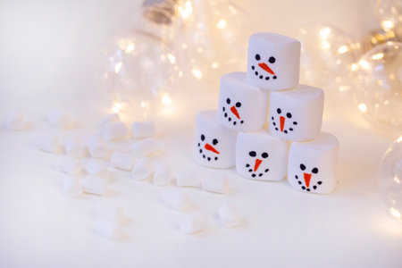 team of marshmallow snowmen on a beige background in the lighting of a garland close-upの写真素材