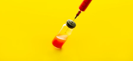 disposable syringe with red liquid and a bottle of medicine on a yellow background, close-upの写真素材