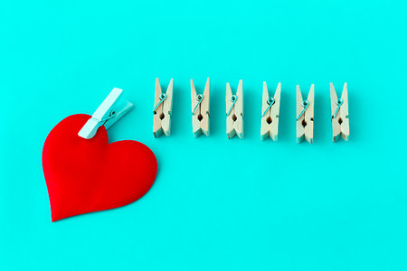 love symbol, heart with a white clothespin and other clothespins on a turquoise background, concept...