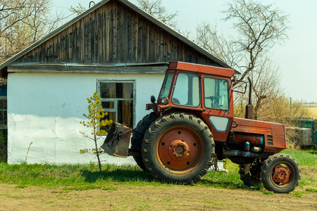 a red tractor parked outside a white farmhouse in early springの写真素材
