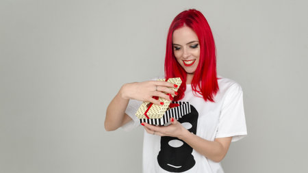 Joyful girl with red hair on a white background. Girl opens a gift