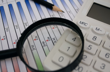 Magnifying glass on a calculator and tables. Focus on the calculator.の写真素材