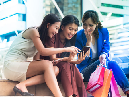 Three happiness asian women are interesting some contents from smart phone.  The one hold her shopping bags. Friendship and lifestyle concept.の写真素材