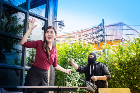 The thief under black mask is intimidating for extortion a beautiful woman's handbag. She was shocked and yelling for help. Threatening situation conceptの写真素材