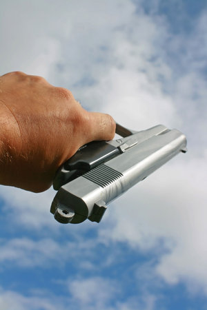 A hand gun pointed upwards towards a sky backgroundの写真素材