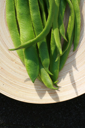 Detail of freshly picked organic runner beans, set on an oval wood grained platter.