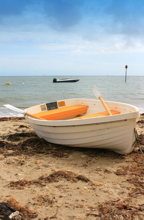 White and Yellow boat on sandy beach. Beach with washed up seaweed, sea horizon in background. Location Christchurch, Dorset UK.の写真素材