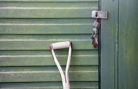 A Garden fork leaning up against a green wooden shed with a bunch of keys hanging from the shed doorの写真素材