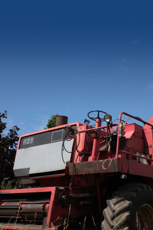 The front end of a red combine harvester machine stationary in a farm field in rural Wiltshire, England, set against a blue summer sky.の写真素材