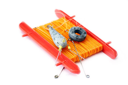 An orange nylon crab line on a red plastic frame with lead weights and hooks set on an isolated...