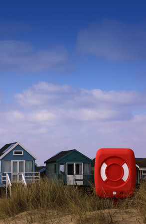 A red beach lifebuoy in front of a row of wooden beach huts. Location in Chritschurch, Hampshire UK. Set on a portrait format with room for copy above.の写真素材