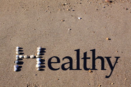 An upper cased letter 'H' formed by beach pebbles on the sand. The word healthy is spelt out by the addition of shadowed text.の写真素材