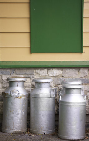 Four old tin and alluminium milk churns set in front of a wooden clad building. Located in an old railway platform in Devon, England. Part of the historical Swanage Railway system.の写真素材