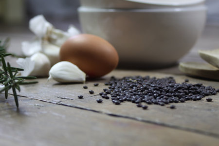 Close up detail of kitchen ingredients comprising of a brown egg, garlic, fresh rosemary and black lentils. All set on a landscape format against a wooden background.の写真素材