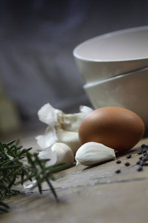 Close up detail of some kitchen ingredients comprising of a brown egg, garlic, fresh rosemary and...