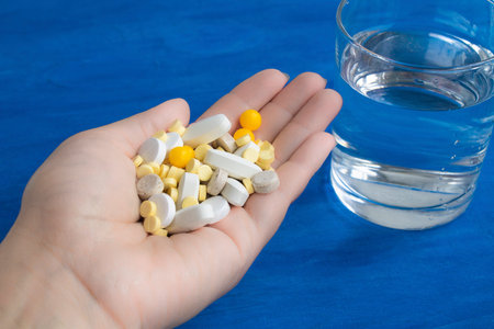 A lot of pills in the hand. Glass with water on the table, blue background
