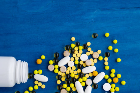 multi-colored pills pour out of a white jar, pills on a blue backgroundの写真素材